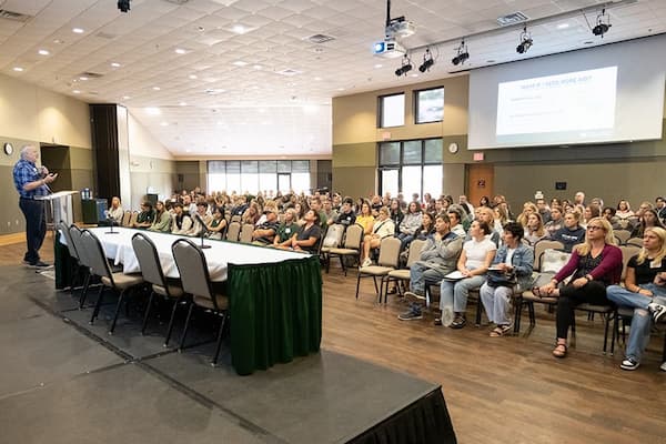 Los estudiantes y las familias se reúnen para una presentación en un evento de visita.