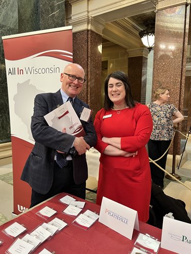 Two people smile at All In Wisconsin booth