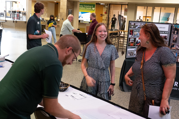 A student and parent stop at a table for information during a GB Orientation session