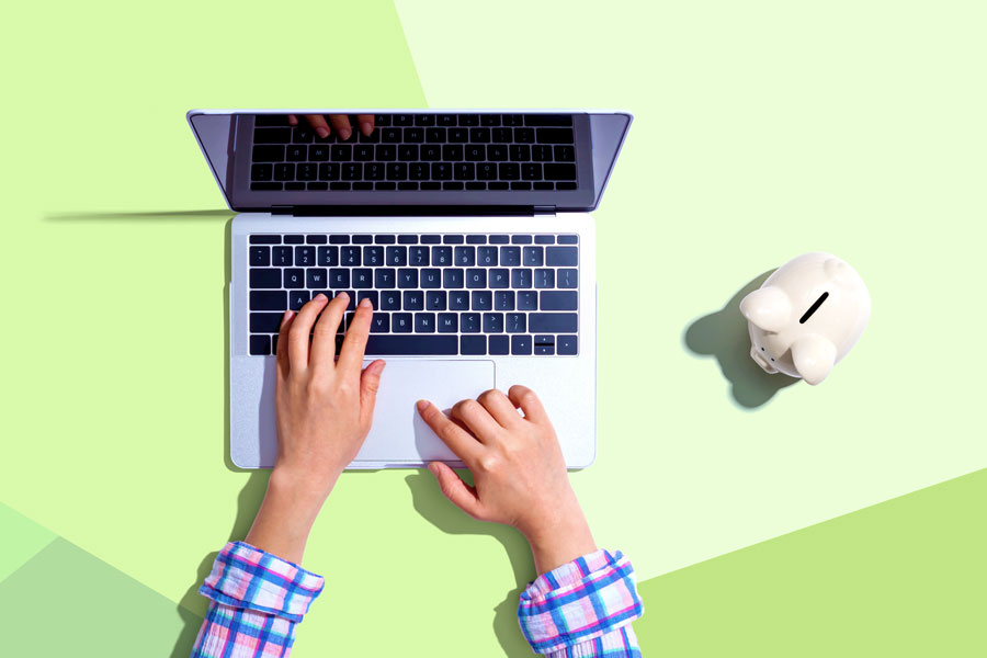 Hands typing on laptop with with piggy bank on table