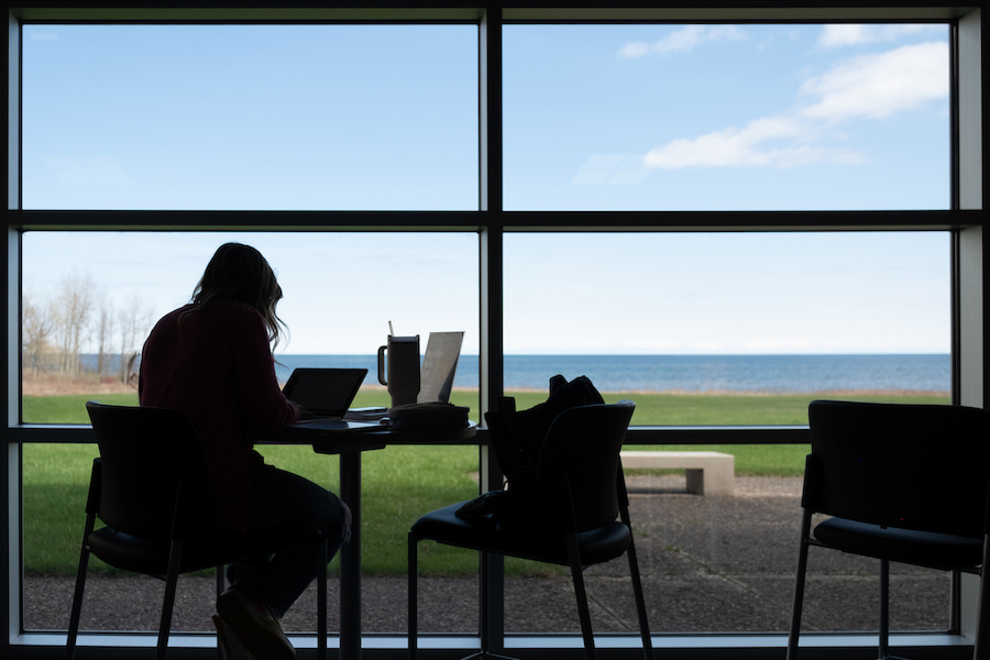 student sitting at table overlooking lakeshore at Manitowoc campus